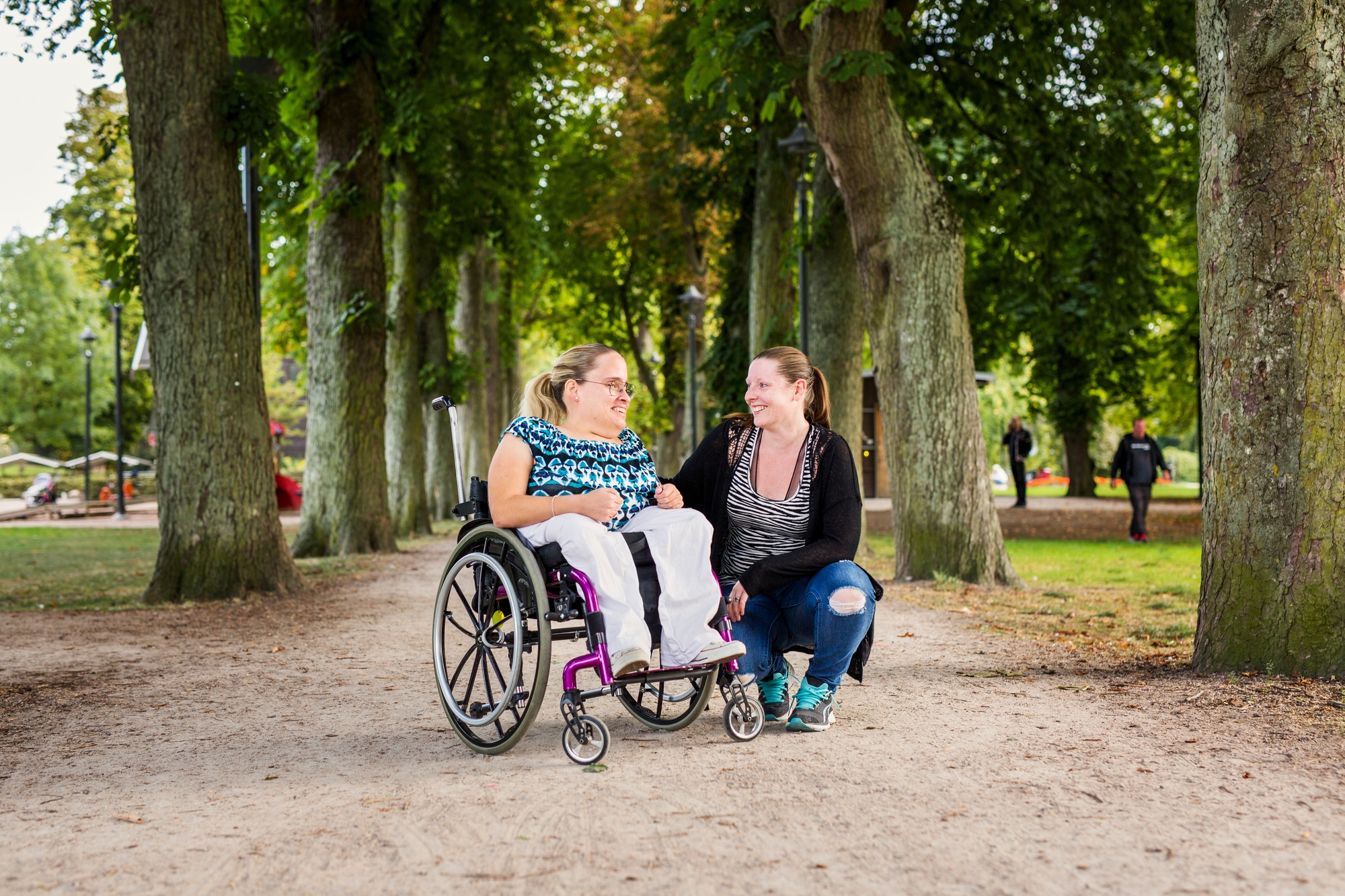 Portrait of disabled woman in wheelchair with assistant in park