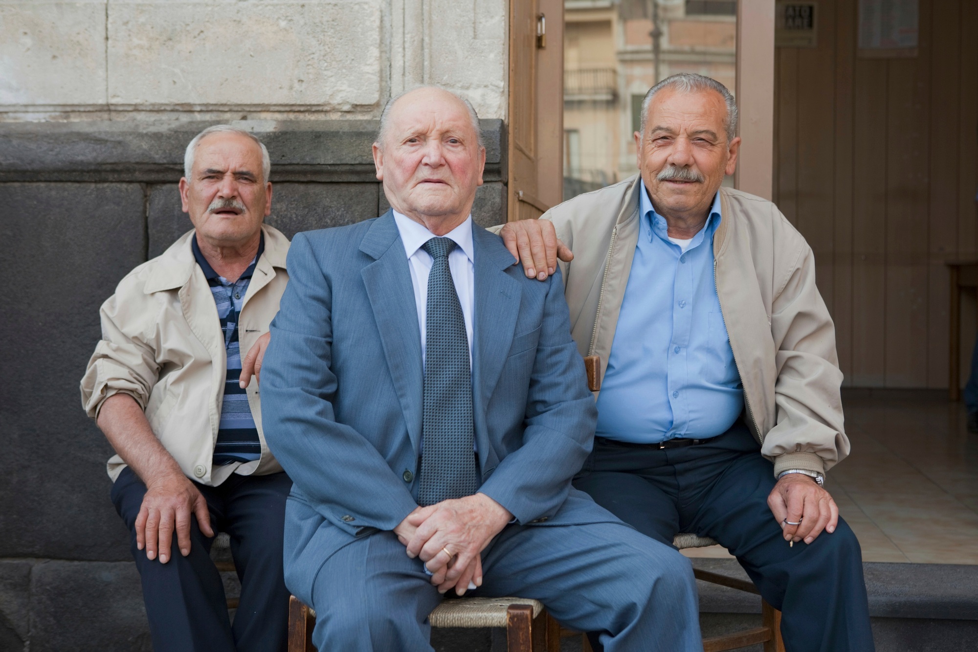 tree old men sitting outside on chairs